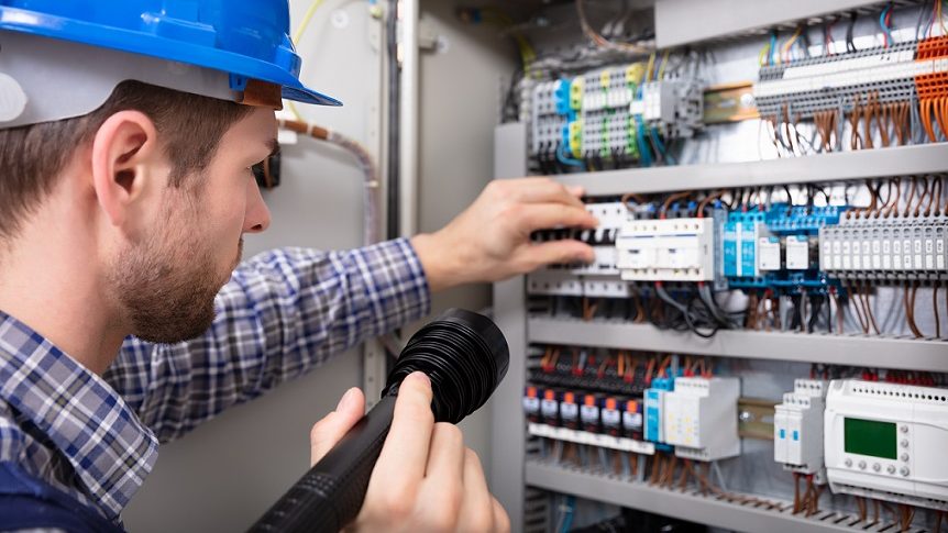 Close-up Of A Electrician Examining A Fuse Box With A Torch